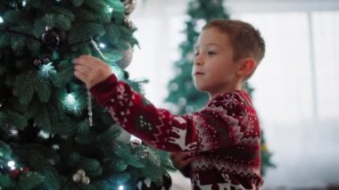 Bir çocuk Noel ağacını süsleyerek süslüyor. Mutlu bir çocukluk, Noel Baba 'nın gelişine hazırlık dekore edilmiş bir odada şenlikli bir atmosfer. Yüksek kalite 4k görüntü