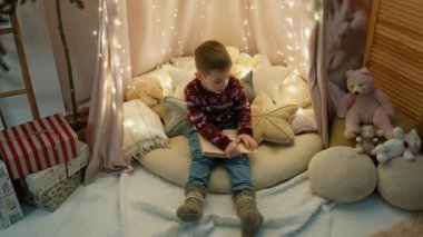 Büyüleyici Noel Anları: Harika dekore edilmiş bir çocuk odasında Büyülü Tatil Hikayeleri okumaya dalmış kürekli küçük bir çocuk. Yüksek kalite 4k görüntü