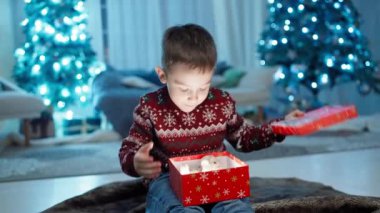 Noel Zevki: Noel Dekoru Altında Mutlu, Gülümseyen Çocuk Tarafından Duygusal Bir Hediye Kutusu Açılışı. Yüksek kalite 4k görüntü