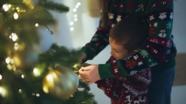 Bir anne oğlunun Noel ağacına bir süs asmasına yardım eder. Mutlu bir aile Noel Baba 'nın gelişi ve yeni yıl kutlaması için hazırlanıyor. Yüksek kalite 4k görüntü