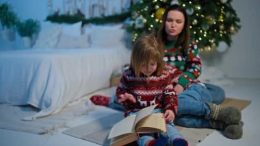 Büyüleyici Hikayeler: Anne ve Çocuklar Ağacın Altında Noel Hikayeleri Okurlar, Evde Tatil Dekorasyonları ile Bir Bayram Atmosferi Oluştururlar. Yüksek kalite 4k görüntü