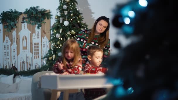 魔法のクリスマスの願い ママは喜びの休日のために木によってサンタに手紙を描く子供を助けます 高品質の4K映像 — ストック動画