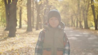 Sonbahar parkında okula yürüyen bir çocuğun portresi. Çocuğun ders almak için acelesi var. Yüksek kalite 4k görüntü