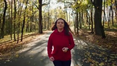 Fat woman jogging in the autumn forest doing fitness. A girl does sports to lose weight. High quality 4k footage
