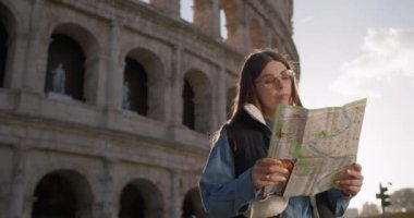 Bir kadın turist Roma Kolezyumu yakınlarındaki bir haritaya bakıyor. Güzel bir kız sokaklarda yürüyor, tarihi mimariye bakıyor ve eğlenceli bir tatil geçiriyor. Yüksek kalite 4k görüntü