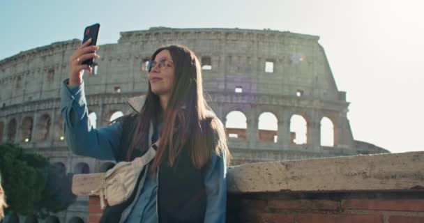 女性は背景としてコロッセオの壮大なファサードでセルフィーをキャプチャし 空を楽しんで ローマの街で彼女の旅行の冒険を反映しています 観光の完璧な瞬間 — ストック動画