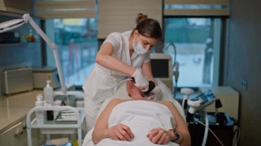 Bir kozmetikçi klinikte bir kadına güzellik prosedürleri uygular. Yaşlı kadınlar için yenileme prosedürleri. Yüksek kalite 4k görüntü
