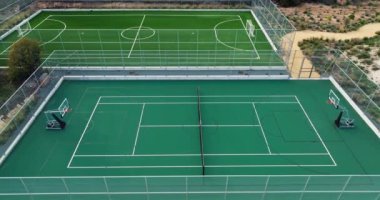 Dağ manzarasındaki tenis kortlarının havadan görünüşü. Yeşil çimlerde tenis oynamak için iki kort, sokaklarda aktif bir spor yaşam tarzı. Yüksek kalite 4k görüntü