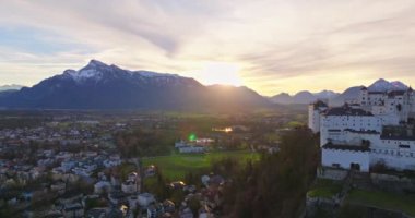Avusturya, Salzburg 'daki Hohensalzburg kalesinin hava manzarası. Gün batımında şehrin tepesindeki bir dağın tepesinde antik mimarisi olan güzel bir kale. Yüksek kalite 4k görüntü