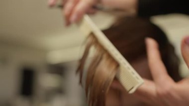 Bir kuaförün yakın çekimi bir tarakla saç çeker ve onu makasla keser. Güzellik salonunda bir profesyonelin kadın saç kesimi. Yüksek kalite 4k görüntü