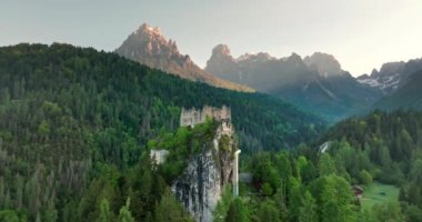 Dolomite Alplerindeki eski bir kalenin havadan görünüşü. Çam ormanındaki bir kayanın tepesindeki bir kale dağ zirveleri ve tepeleri manzarası. Yüksek kalite 4k görüntü