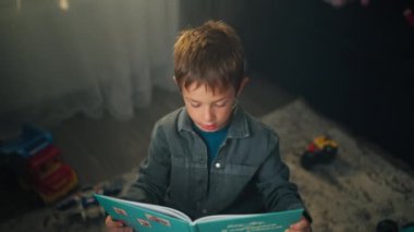 Bir çocuk çocuk çocuk odasındaki oyun masasında bir kitap okuyor. Çocuğun eğitimi ve gelişimi. Yüksek kalite 4k görüntü