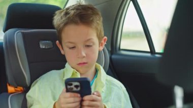 Çocuk telefonda bir video izliyor ve araba sürerken oynuyor. Emniyet kemeri takılı bir çocuk ailesiyle birlikte okula gider. Yüksek kalite 4k görüntü