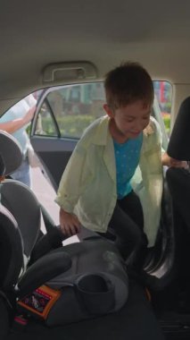 Anne, çocuğuna okula güvenli ve rahat bir yolculuk için araba koltuğuna oturmasında yardım ediyor. Yüksek kalite 4k görüntü