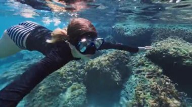 Gözlüklü genç bir kız denizin altında yüzüyor. Aktif eğlence turizmi ve okyanusta şnorkelle yüzme. Yüksek kalite 4k görüntü