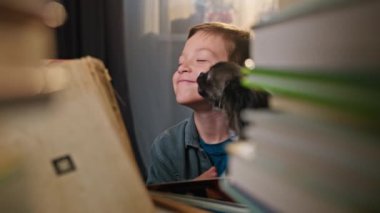 Bir okul çocuğu ev ödevi yaparken bir köpekle oynar. Çocuk gülümseyerek ve mutlu bir şekilde evcil hayvanla eğleniyor. Yüksek kalite 4k görüntü