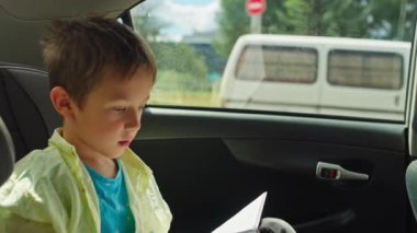 Okul çağındaki çocuk, okula giden yolda ya da aile yolculuğunda ebeveynleriyle seyahat ederken çocuk emniyet koltuğunda kitap okuyor. Yüksek kalite 4k görüntü