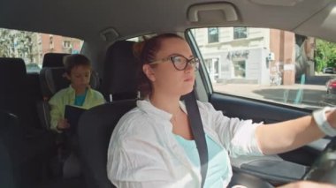 Oğlu çocuk oto koltuğunda kitap okurken annesi araba sürüyor. Bir okul çocuğu ailesiyle birlikte arabayla okula gider. Yüksek kalite 4k görüntü