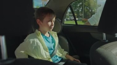 Bir anne, oğlunun arabadan inmesine yardım eder. Çocuk emniyet kemerini çözdü ve çocuk oto koltuğundan indi. Yüksek kalite 4k görüntü