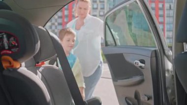 Anne, Oğlu 'nun Araba Koltuğu' na binmesine ve Emniyet kemerini bağlamasına yardım ediyor. Güvenli bir başlangıç için ya da okula yolculuk için. Yüksek kalite 4k görüntü