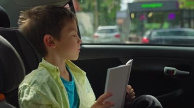 Çocuk Araba Koltuğu 'nda kitap okuyan öğrenci ebeveynler okula giderken ya da seyahat sırasında aile gezisinde öğrenim görürken. Yüksek kalite 4k görüntü