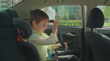 Çocuk emniyet kemerini çözdü ve çocuk oto koltuğundan indi. Bir anne, oğlunun arabadan inmesine yardım eder. Yüksek kalite 4k görüntü