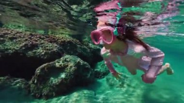 Kız çocuğu suyun altında yüzer ve şnorkelle yüzer. Çocuk gözlük takıp okyanusa dalıyor ve sualtı dünyasına bakıyor. Yüksek kalite 4k görüntü