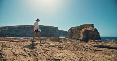 Okyanus kıyısında yürüyüş yapan bir kadının yavaş çekim videosu. Doğanın, turizmin ve seyahatin güzel manzarasında deniz dalgalarının çarptığı bir kayanın üzerinde yürüyen bir kız. Yüksek kalite 4k görüntü