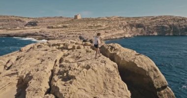 Okyanus kıyısındaki bir uçurumun tepesine tırmanan bir kadının hava görüntüsü. Yürüyüş ve turizm, güzel deniz manzaralarına geziler, dinlenme ve özgürlük hissi. Yüksek kalite 4k görüntü