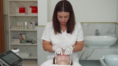 Kozmetik uzmanı kremi uyguluyor ve ameliyattan sonra kadınların yüzüne sürüyor. Yüzün derisini yüzmek, güzellik prosedürleri ve kendine bakım. Yüksek kalite 4k görüntü