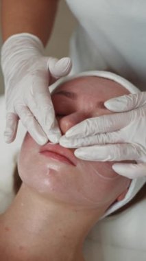 Kozmetolojide bir güzellik uzmanı, bir kadının yüzüne krem sürer. Bir kızın cildine ve güzelliğine önem vermek, bir profesyonelin güzellik prosedürleri. Yüksek kalite 4k görüntü