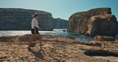 Kayalık okyanus kıyısında bir kayanın üzerinde yürüyen bir kadının yavaş çekim videosu. Güzel doğal manzaralarda yürüyüş ve turizm. Yüksek kalite 4k görüntü