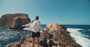 Okyanus kıyısında bir kayanın üzerinde yürüyen bir kadının yavaş çekim videosu. Deniz dalgalarının kıyıya vurması, Akdeniz 'deki seyahat ve turizm videoları. Yüksek kalite 4k görüntü