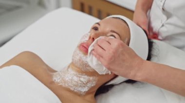 Bir klinikte gelişmiş güzellik tedavileri ve cilt bakımı için anesteziyi kaldırmak için hastanın yüzünü temizleyen kozmetolog. Yüksek kalite 4k görüntü