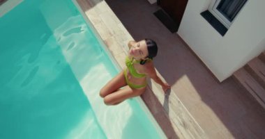 Havuz kenarında güneşlenen güzel bir kadın mayo ve güneşli bir tatilde ayaklarıyla su sıçratan bir villada güneşleniyor. Yüksek kalite 4k görüntü