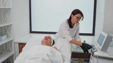 Bir kozmetolog güzellik aletini kozmetolojide bir prosedüre göre ayarlar. Kozmetik, güzellik ve sağlık, cilt bakımı randevusu olan bir kadın. Yüksek kalite 4k görüntü