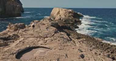 Gozo Island Malta 'daki Rocky Shore of Mantar Kayası' nda Yürüyen Kadın 'ın Havadan Görüntüsü. Kıyı şeridine dalgalar çarpıyor. Yüksek kalite 4k görüntü