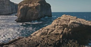 Deniz kıyısında kayaya tırmanan bir kızın hava görüntüsü. Okyanus dalgalarının kıyılardaki taşlara çarptığı sahilde dünyanın sonunun, turizmin ve gezgin kızın destansı videosu..
