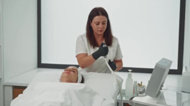 Güzellik uzmanı, kadın bir hastaya ışıltılı çözümler sunarak güzellik prosedürü uygular. Yüz bakımı ve güzellik kozmetolojisi prosedürleri. Yüksek kalite 4k görüntü