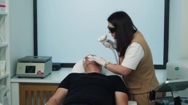 Bir kozmetolog, yaşlı bir adamın yüz derisini cihazla temizliyor. Orta yaşlarda güzellik ve erkek sağlığı. Yüksek kalite 4k görüntü