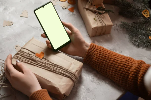 stock image a young woman holds a phone, a tablet in her hand and fulfills an order by phone, taking an order for gift wrapping, in the background a Christmas tree and lights, the concept of preparing for the new year, merry christmas, new year 2023