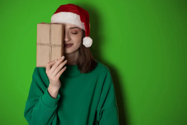 young woman in a green sweater and in a New Year\'s hat holds a gift box on a simple green background. Holiday concept Happy New Year 2023, chrome key, merry christmas