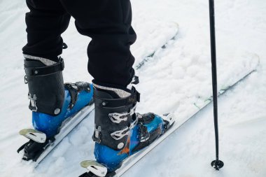 Close-up of the leg of a skier athlete in ski boots goes up on skis against the backdrop of snow-capped mountains on a sunny day. Winter sports concept