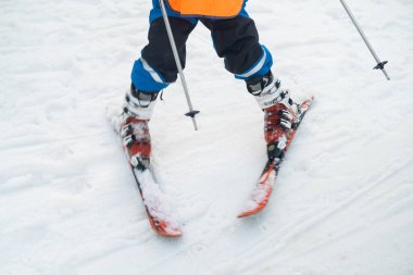 Close-up of the leg of a skier athlete in ski boots goes up on skis against the backdrop of snow-capped mountains on a sunny day. Winter sports concept
