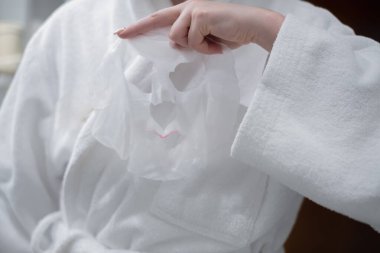 Woman with a sheet mask in her hands in the bathroom before applying it to her face