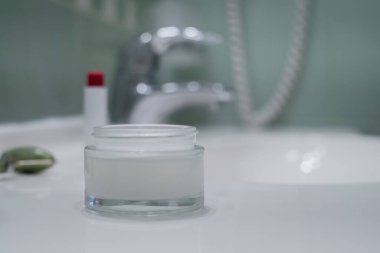 Face cream, face roller and lipstick near the sink on the counter in the bathroom, space for text