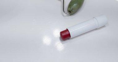 Face cream, face roller and lipstick near the sink on the counter in the bathroom, space for text