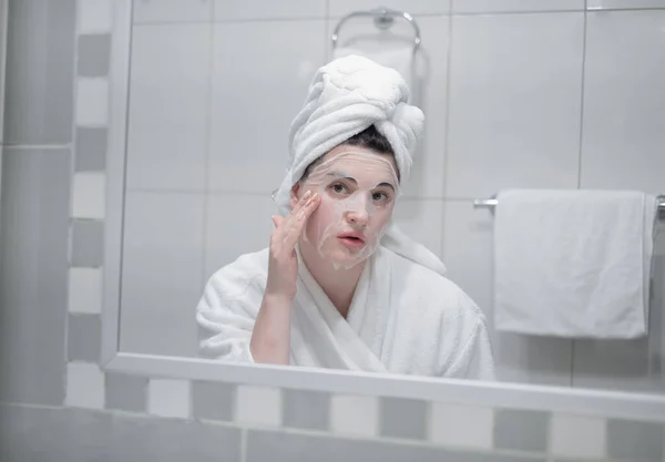 Young Caucasian Woman White Bathrobe Towel Her Head Removes Moisturizing — стоковое фото