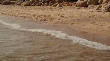 slow motion of foamy waves rolling towards white sand beach under low sunlight