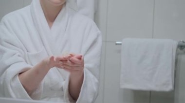 Kız ellerini krem sürmüş ve masaj yapmış, beyaz bir bornoz, banyo, el bakımı, nemlendirici cilt kremi, yakın çekim